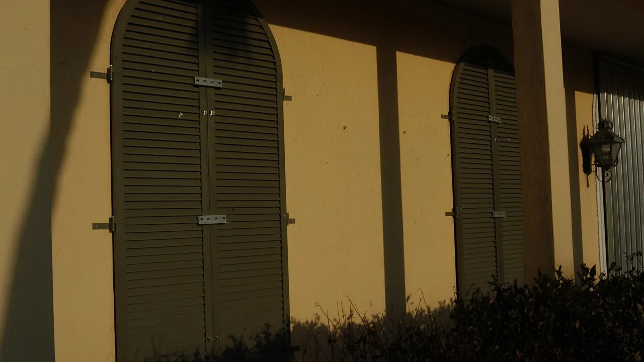 Louvered Bahama-style shutters closed over arched windows